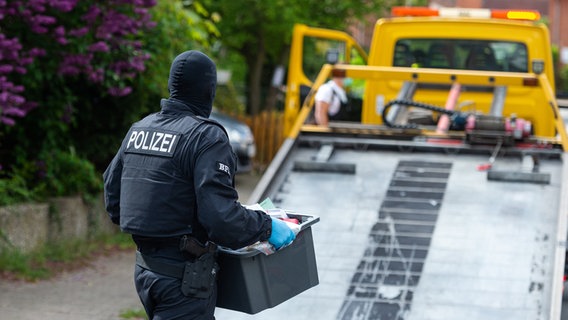 Ein maskierter Polizist trägt eine Kiste an einem Abschleppwagen vorbei. © dpa-Bildfunk Foto: Philipp Schulze