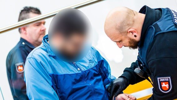 Ein Justizmitarbeiter löst bei einem der beiden Angeklagten bei Prozessauftakt in einem Saal vom Landgericht Hannover nach einem Mord in einem Autohaus die Handschellen. © picture alliance/dpa | Moritz Frankenberg Foto: Moritz Frankenberg
