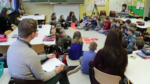 Lehramtsstudenten sitzen gemeinsam mit Schülern einer 4. Klasse in einem Klassenraum. © NDR Foto: Jens Otto