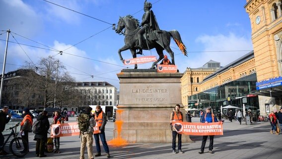 Aktivisten der Letzten Generation demonstrieren vor und auf dem Ernst-August-Denkmal vor dem Hauptbahnhof in Hannover mit Plakaten und Farbbeuteln. © Julian Stratenschulte/dpa Foto: Julian Stratenschulte