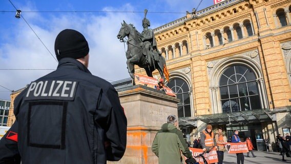 Aktivisten der Letzten Generation demonstrieren vor und auf dem Ernst-August-Denkmal vor dem Hauptbahnhof in Hannover mit Plakaten und Farbbeuteln. © picture alliance/dpa Foto: Julian Stratenschulte
