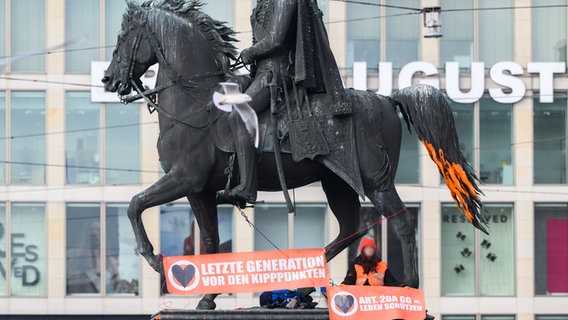 Aktivisten der Letzten Generation demonstrieren vor und auf dem Ernst-August-Denkmal vor dem Hauptbahnhof in Hannover mit Plakaten und Farbbeuteln. © dpa-Bildfunk Foto: Julian Stratenschulte