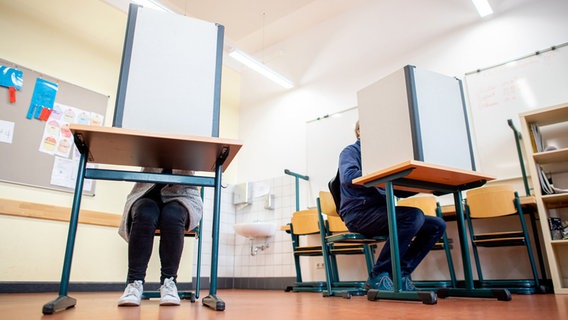 Wähler sitzen in einem Wahlraum in der Lutherschule hinter einem Sichtschutz. © Hauke-Christian Dittrich/dpa Foto: Hauke-Christian Dittrich/dpa