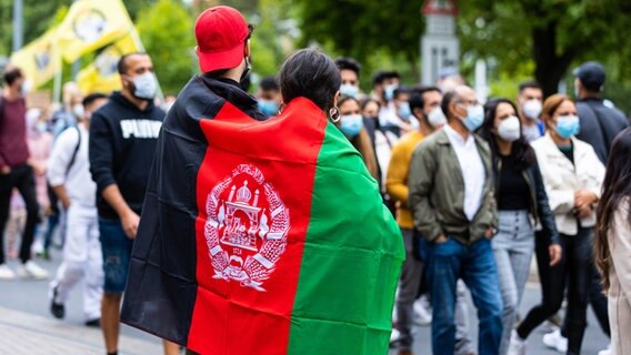Eine Frau und ein Mann stehen am Rand des Demonstrationszuges. Sie sind beide in eine Afghanistan-Flagge eingehüllt. © picture alliance / Fotostand Foto: Matthey