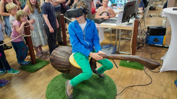 Ein Junge sitzt auf einem "fliegenden Besen" mit einer Virtual-Reality-Brille bei der Maker Faire Hannover 2015 © picture alliance / dpa | Julian Stratenschulte Foto: Julian Stratenschulte