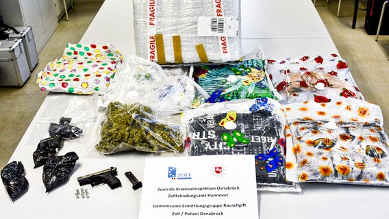 Tüten mit Drogen (Marihuana) und eine Waffe auf einem weißen Tisch (Sicherstellung des des Zollfahndungsamts Hannover und der Zentralen Kriminalinspektion Osnabrück). © Zollfahndungsamt Hannover 