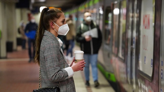 Eine Frau steht mit FFP2-Maske am Bahnsteig. © imago/Die Videomanufaktur/Martin Dziadek 