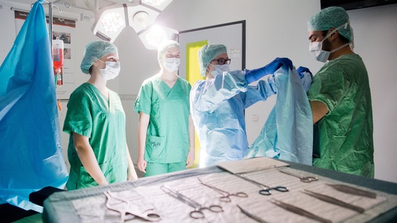 Medizinstudenten üben in einem nachgebildeten OP-Raum das hygienisch korrekte Anlegen eines OP-Kittels. © picture alliance/dpa Foto: Julian Stratenschulte