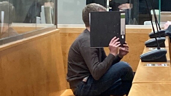 Ein Angeklagter bedeckt in einem Gerichtssaal sein Gesicht mit einem Aktenordner. © dpa-Bildfunk Foto: Christina Sticht