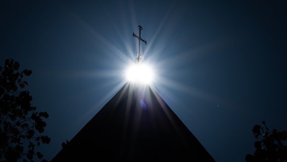 Die Sonne strahlt unter einem Kreuz auf dem Dom Osnabrück. © picture alliance/dpa | Friso Gentsch Foto: Friso Gentsch