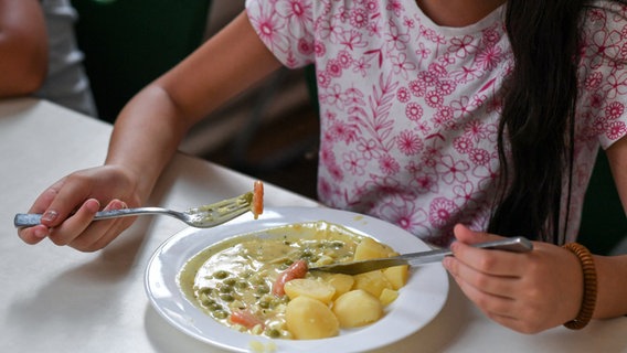 Ein Mädchen sitzt in einer Kantine vor einem Teller mit Essen. © dpa Foto: Jens Kalaene