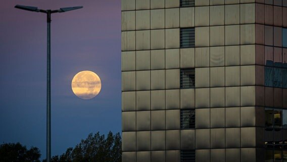 Der Mond zwischen einem Hochhaus und einer Laterne. © Moritz Frankenberg/dpa Foto: Moritz Frankenberg/dpa