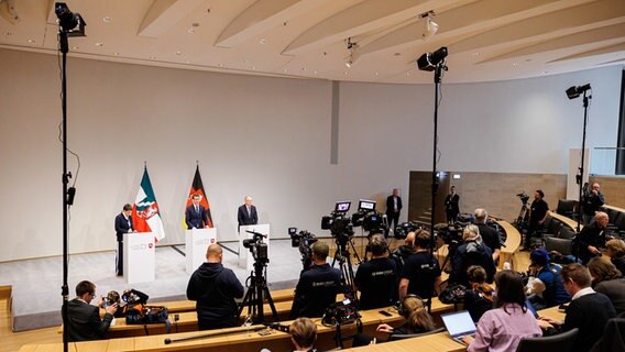 Journalisten stehen und sitzen im Auditorium vom Schloss Herrenhausen während der Abschluss-Pressekonferenz zur Ministerpräsidentenkonferenz mit Hendrik Wüst (2.v.r, CDU), Ministerpräsident von Nordrhein-Westfalen, und Stephan Weil (3.v.r, SPD), Ministerpräsident von Niedersachsen. © dpa-Bildfunk Foto: Michael Matthey