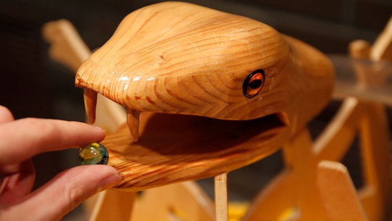 Eine Murmel wird ins Maul einer Schlange aus Holz gesteckt. © NDR Foto: Henning Martin