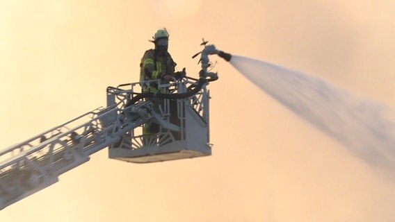 Eine Einsatzkraft der Feuerwehr steht zum Löschen eines Brandes in einem Malerbetrieb auf einer Drehleiter. © TeleNewsNetwork 