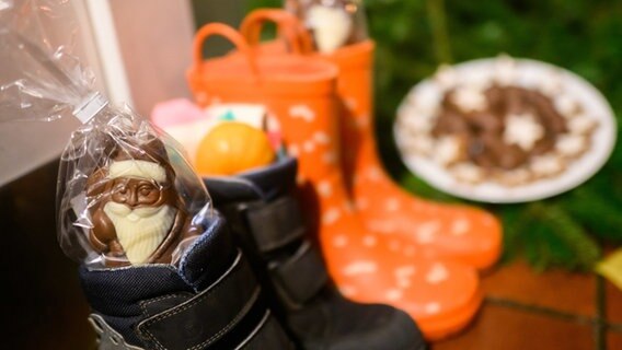 Kinderstiefel, gefüllt mit Schoko-Nikoläusen, Mandarinen und weiteren Sachen, stehen vor einer Haustür eines Einfamilienhauses in der Region Hannover. © dpa-Bildfunk Foto: Julian Stratenschulte
