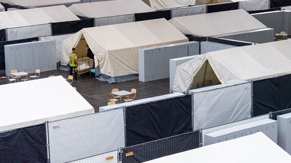Feuerwehrleute tragen ein Babybett in ein Zelt. © dpa Foto: Lino Mirgeler