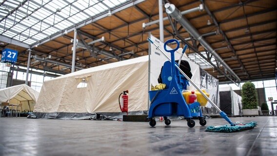 Ein Wischmop steht vor einem Zeltdorf in einer Messehalle. © dpa Foto: Lino Mirgeler