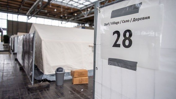 Ein Mehrsprachiges Schild weist auf die Nummer des Flüchtlingsdorfes hin. © dpa Foto: Lino Mirgeler
