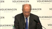 Hans Dieter Pötsch sitzt vor einem Aufsteller auf dem "Volkswagen" steht. © NDR 