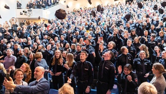 Nienburg: Polizistinnen und Polizisten vom 18. Bachelorstudienjahrgang der Polizeiakademie Niedersachsen werfen bei ihrer Abschlussfeier im Theater auf dem Hornwerk ihre Polizeimützen hoch. © dpa-Bildfunk Foto: Michael Matthey