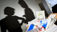 Ein Paket mit Untersuchungsmaterial steht auf einem Tisch, an der Wand sind die Schatten von zwei Frauen. © dpa Bildfunk Foto: Julian Stratenschulte