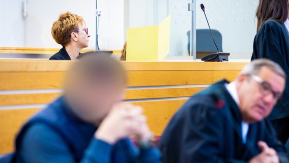 Die beiden Angeklagten (unscharf und hinter einer gelben Mappe) im Prozess um ein mutmaßliches Autorennen in Barsinghausen sitzen im Gerichtssaal im Landgericht Hannover. © dpa Foto: Moritz Frankenberg