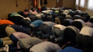 Betende Moslems knien in einem Gebetsraum.  Foto: Screenshot