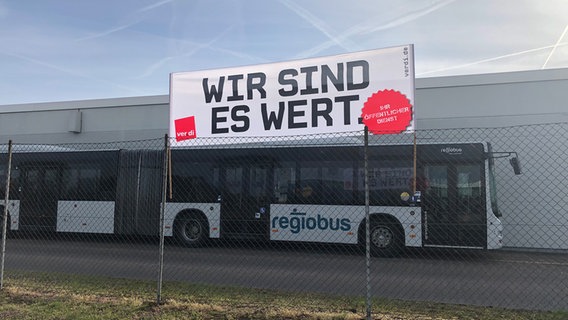 "Wir sind es wert" steht auf einem Plakat vor einem Regiobus (Warnstreik von Regiobus in Hannover). © NDR Foto: Marie Gottschalk