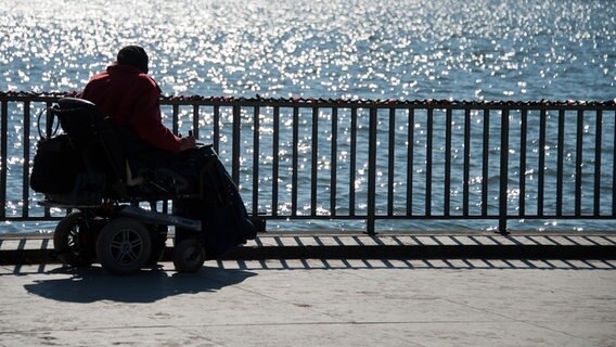 Eine Frau im Rollstuhl blickt auf den Maschsee. Auf dem Wasser spiegelt sich das Licht der Sonne. © picture alliance/dpa/Julian Stratenschulte Foto: Julian Stratenschulte