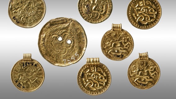 Goldene Amulette und Münzen auf weißem Untergrund. © Landesmuseum Hannover 