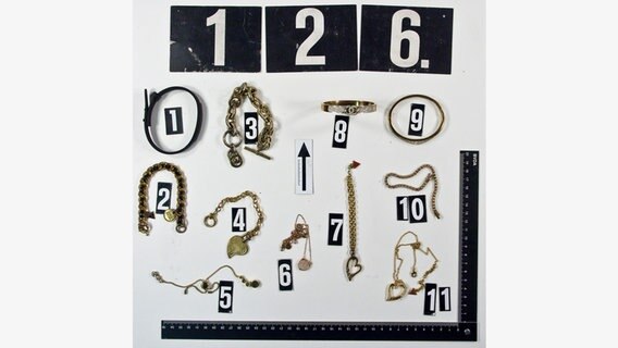 Uhren und Schmuck liegen auf einem Tisch der Polizei mit einem Lineal zum Größenvergleich und mit Nummer geordnet. © Polizeiinspektion Göttingen 