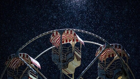 Ein Riesenrad steht im dichten Schneefall am frühen Morgen auf einem Weihnachtsmarkt auf dem Ernst-August-Platz. © Moritz Frankenberg/dpa Foto: Moritz Frankenberg/dpa