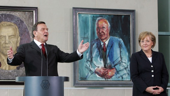 Bei der Übergabe eines Schröder-Porträts spricht der frühere Bundeskanzler Gerhard Schröder im Kanzleramt im Beisein von Bundeskanzlerin Angela Merkel. © dpa-Bildfunk Foto: Rainer Jensen