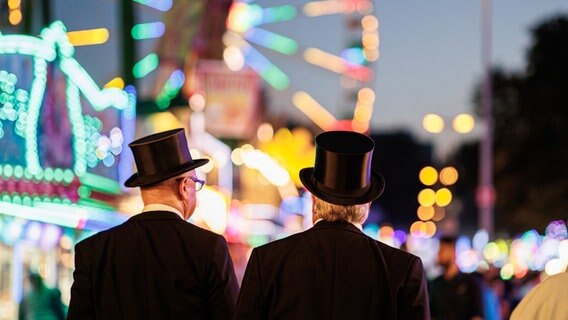 Zwei Personen mit Zylinder-Hüten laufen über das Schützenfest auf dem Schützenplatz. © dpa Foto: Michael Matthey