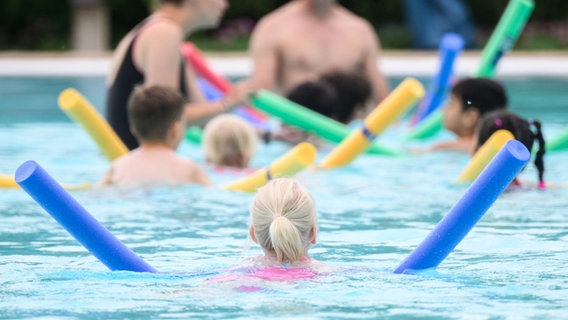 Kinder sind bei einer Schwimmstunde mit Schwimmnudeln im Wasser. © Julian Stratenschulte/dpa Foto: Julian Stratenschulte