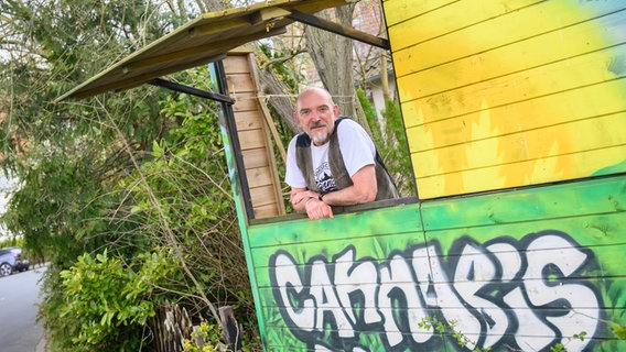 Heinrich Wieker vom Cannabis Socialclub Hannover e.V. steht an seinem Gartenzaun an einer Bretterbude, auf der das Wort Cannabis steht. © dpa-Bildfunk Foto: Julian Stratenschulte