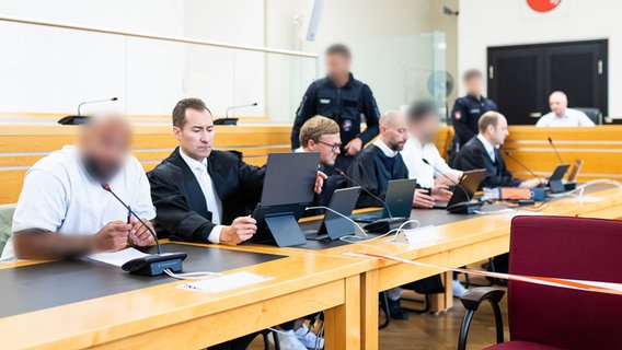 Der angeklagte Staatsanwalt (4.v.r.) und ein weiterer Angeklagter sitzen zum Auftakt eines Prozesses wegen Bestechlichkeit und Verletzung des Dienstgeheimnisses in einem Saal des Landgerichts Hannover. © dpa Foto: Moritz Frankenberg