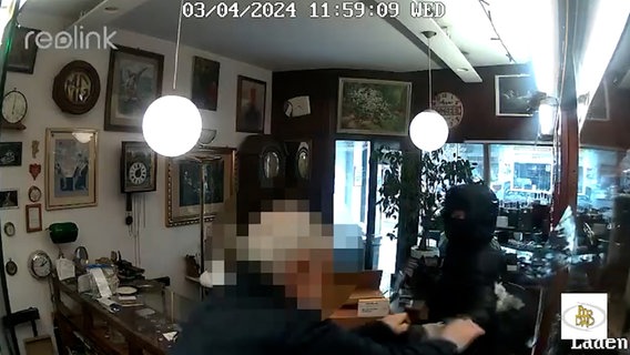 Das Bild einer Überwachungskamera zeigt einen vermummten Mann und einen Ladenbesitzer in einem Juwelier. © Pressestelle Polizei Bremen 