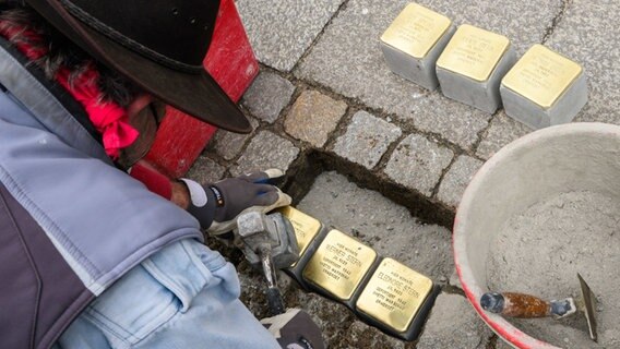 Ein Steinmetz lässt Stolpersteine in einen Gehweg ein. © dpa Foto: Julian Stratenschulte