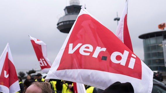 Ein Flughafen-Mitarbeiter streiken vor dem Flughafen in Hannover und halten Verdi-Fahnen in die Luft. © picture alliance 