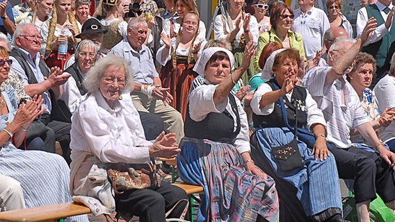 Menschen sitzen auf Bierbänken und winken. © NDR Foto: Frank Tunnat