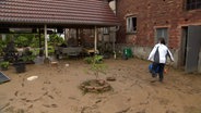 Eine Frau geht über einen von Schlamm überfluteten Hof in Thal nachdem ein Schlammlawine den Ort getroffen hat. © NDR 