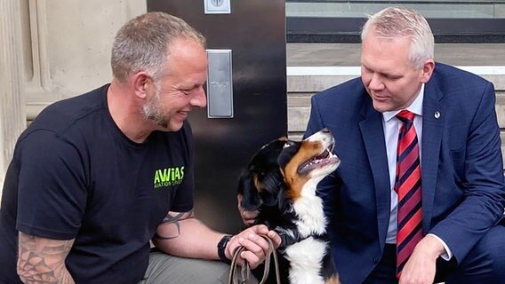 Björn Thümler hockt neben einem Corona-Spürhund der Tierärztlichen Hochschule vor dem Niedersächsischen Landtag. © Niedersächsisches Ministerium für Wissenschaft und Kultur 