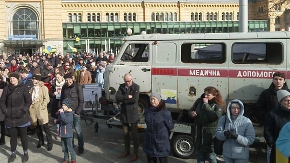 Ein ukrainischer Krankenwagen mit Einschusslöchern steht vor dem Hauptbahnhof Hannover. Es findet eine Demonstration mit zahlreichen Menschen statt. © NDR 