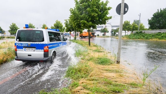 Ein Polizeibus fährt über die überflutete Hermesallee am Messegelände. © dpa Foto: Julian Stratenschulte