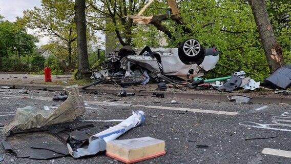 Eine Straße ist mit Glassplittern übersät nach einem Unfall, der sich bei einer Verfolgungsjagd mit der Polizei ereignet hat, ein Auto liegt an einem Baum auf dem Dach. © TNN/dpa Foto: TNN