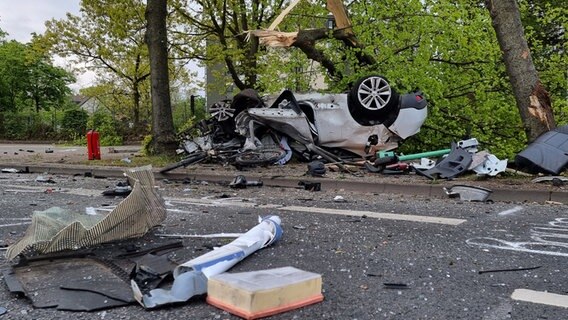 Eine Straße ist mit Glassplittern übersät nach einem Unfall, der sich bei einer Verfolgungsjagd mit der Polizei ereignet hat, ein Auto liegt an einem Baum auf dem Dach. © TNN/dpa Foto: TNN