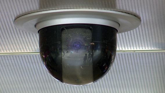In der Linse eines Überwachungskamera spiegeln sich Personen in einem Bahnhof. © NDR 