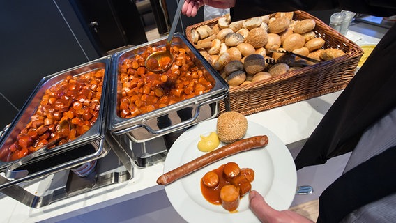 Ein Mann nimmt sich während der Volkswagen AG Hauptversammlung Currywurst von einem Buffet. Ein Mann nimmt sich während der Volkswagen AG Hauptversammlung Currywurst von einem Buffet. © dpa Foto: Silas Stein